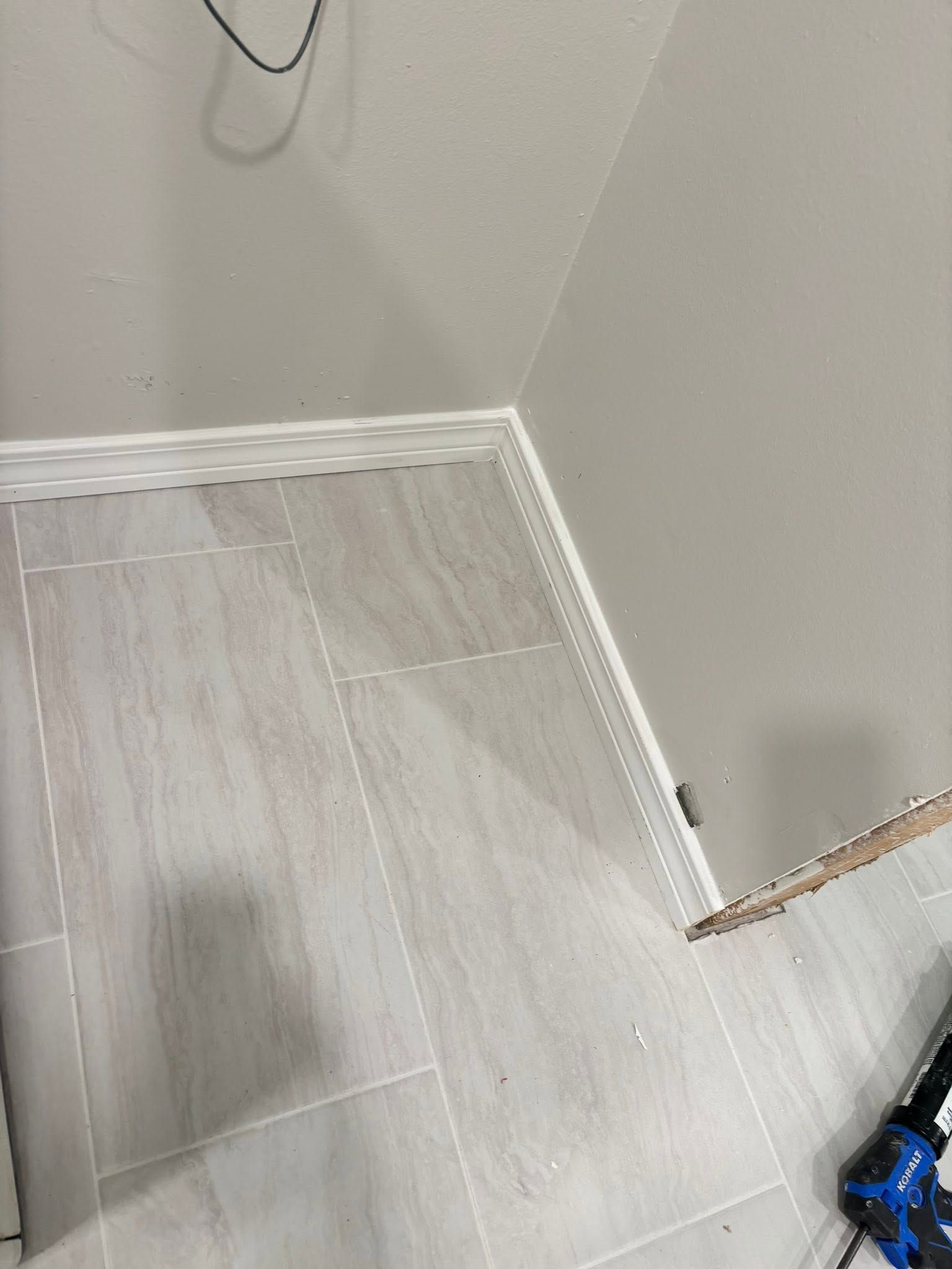 Empty corner of a room with white walls, light wood floor, and a small gap near the baseboard