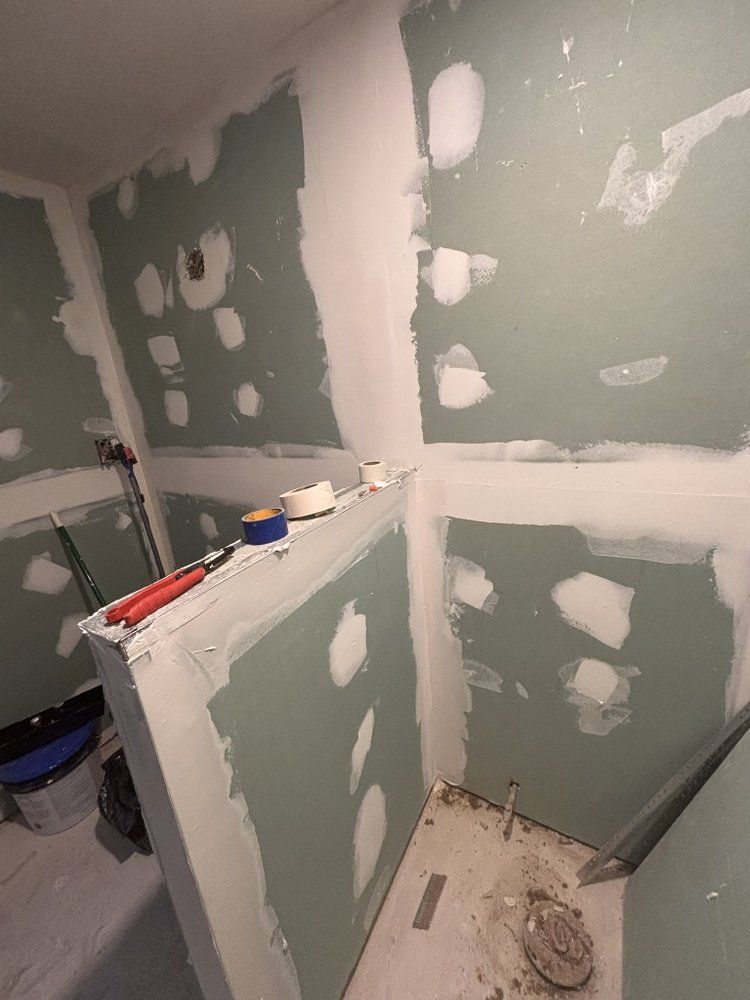 Unfinished bathroom with green drywall, white joint compound patches, and tools on a half-built wall.