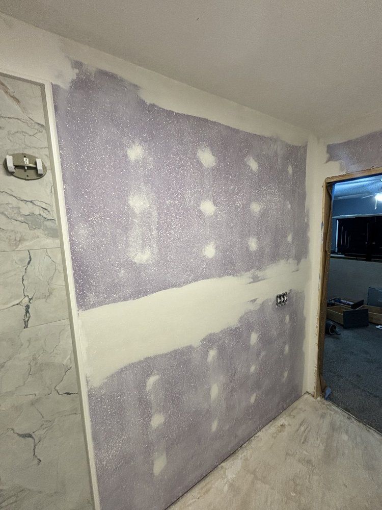 Partially drywalled interior wall with purple and white joint compound in a room under renovation