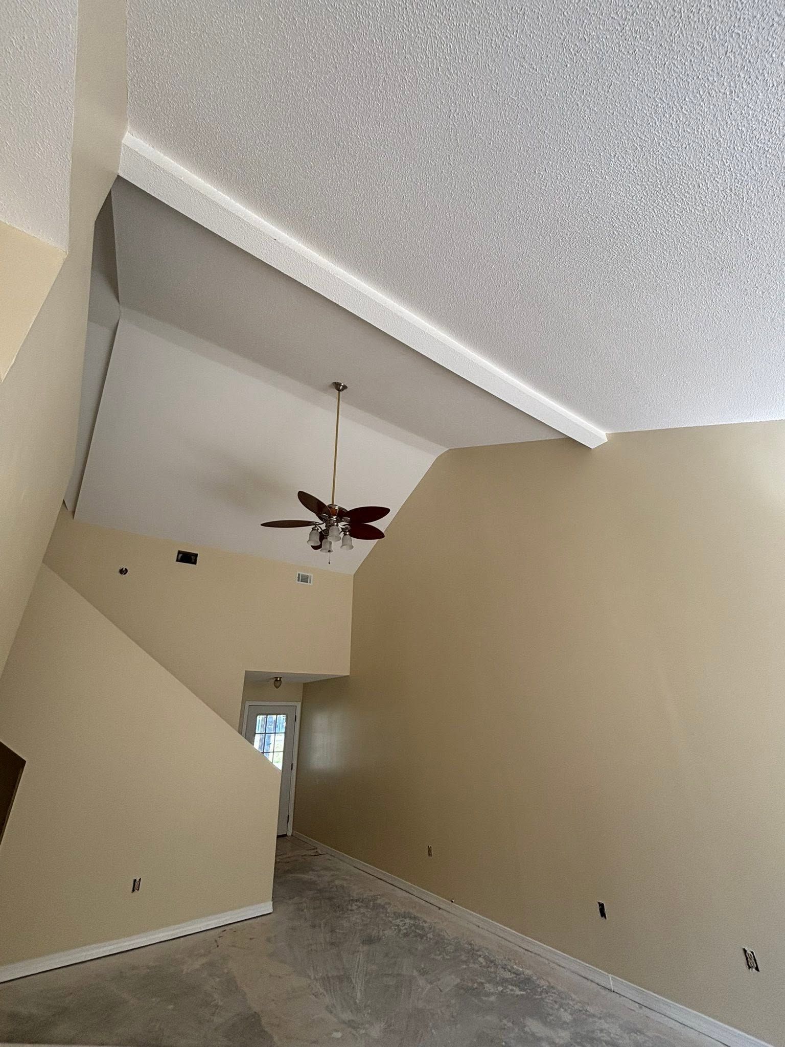 Tall beige hallway with a vaulted ceiling, ceiling fan, and tiled floor leading to a doorway.