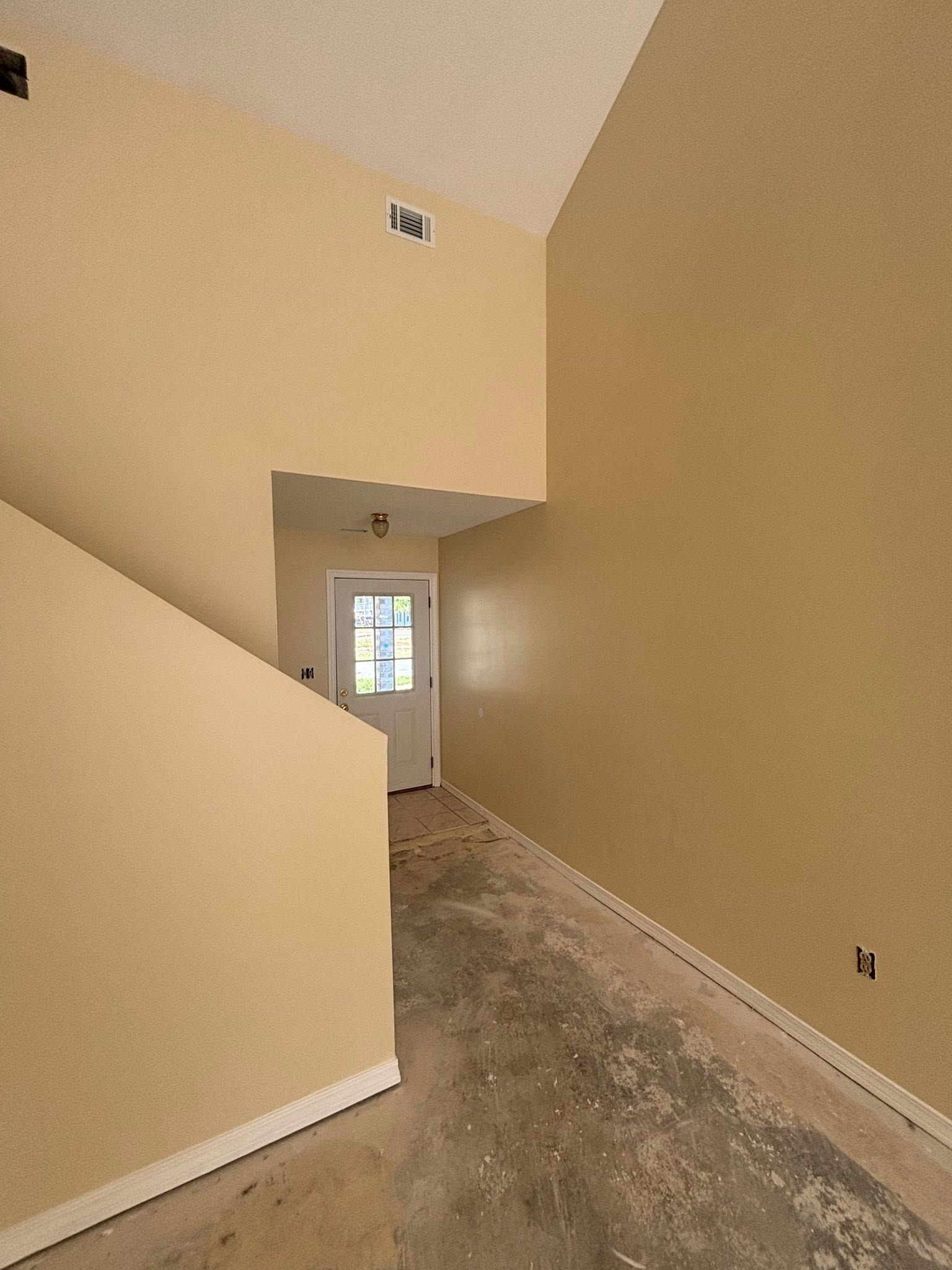 Empty beige hallway with carpeted stairs and a front door in the distance