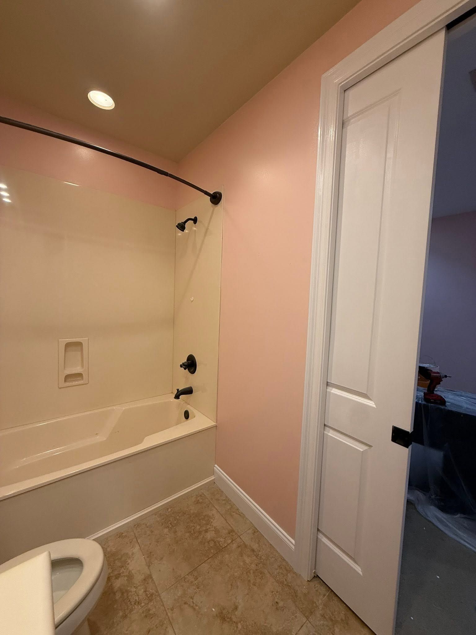 Bathroom with a shower tub, beige walls, white door, and visible toilet seat.