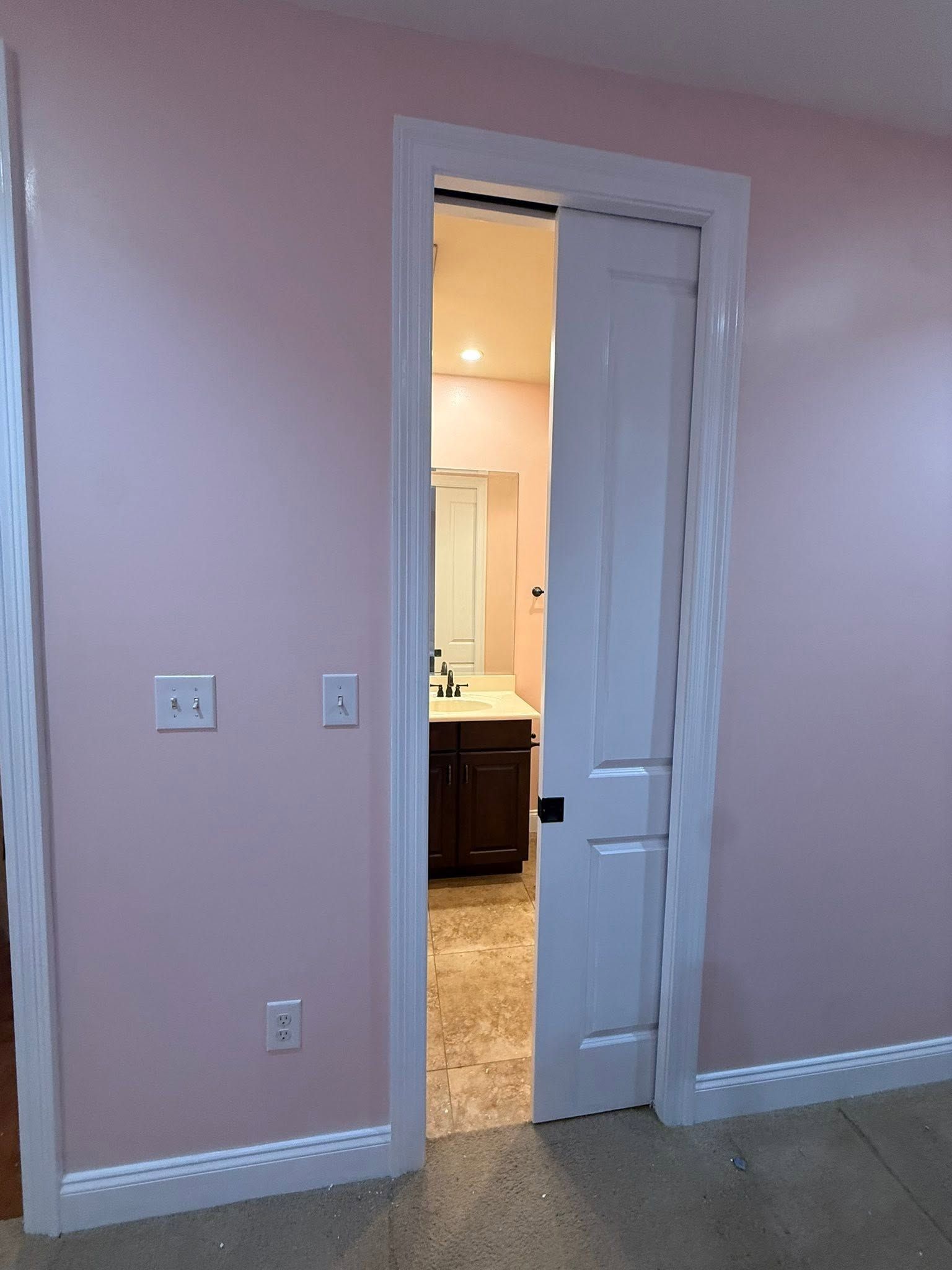 Pink wall with a doorway opening into a lit room with a sink and vanity visible.