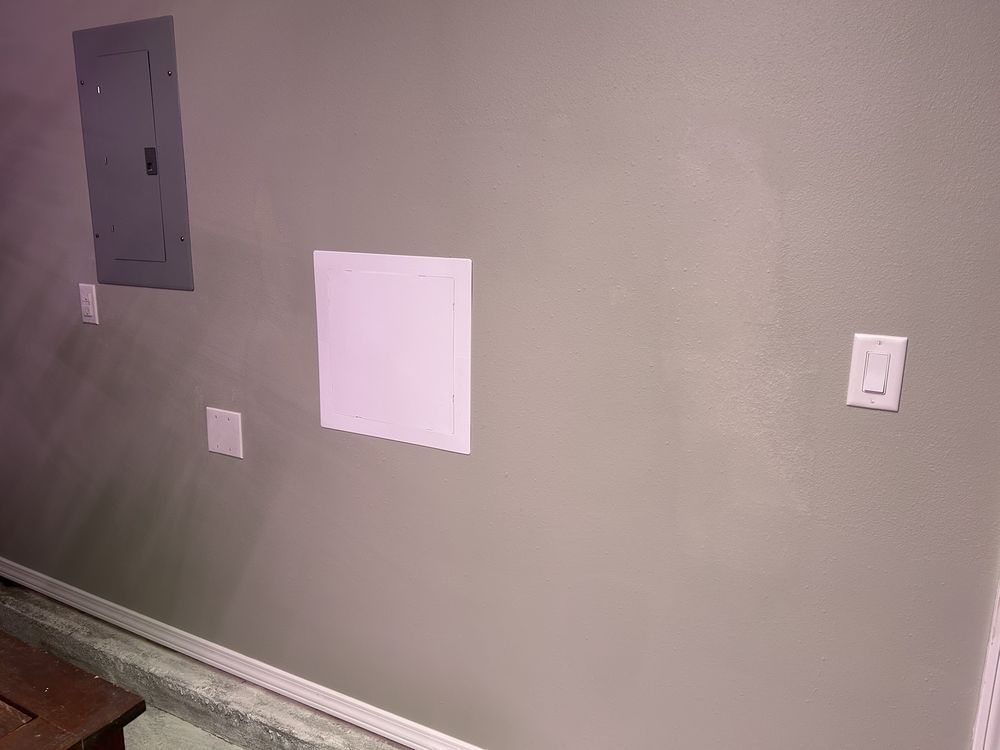Empty wall with electrical panels and outlets, plus a small white patch and baseboard trim.