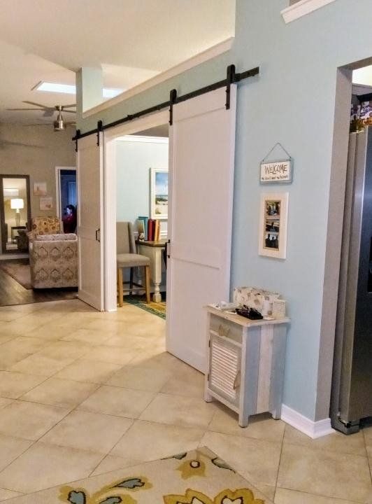 Bright hallway with white barn doors, pale blue walls, tiled floor, and small decor table by a rug