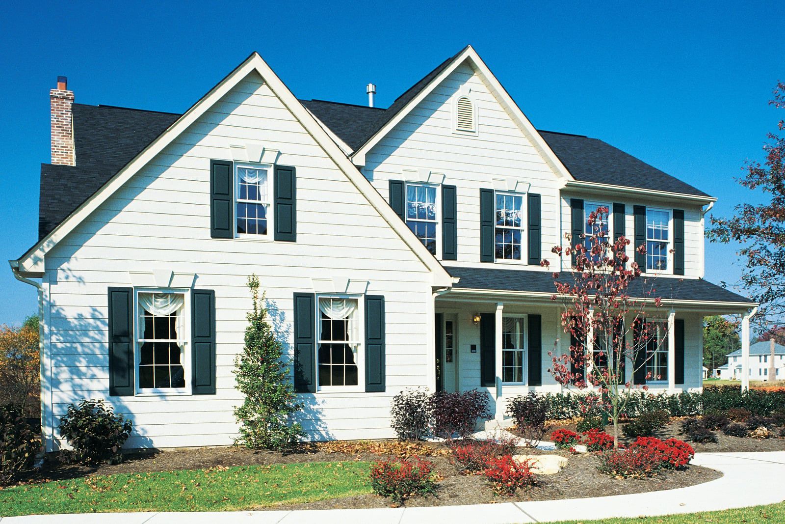 Single-story beige house with patio, large windows, and green lawn on a sunny day