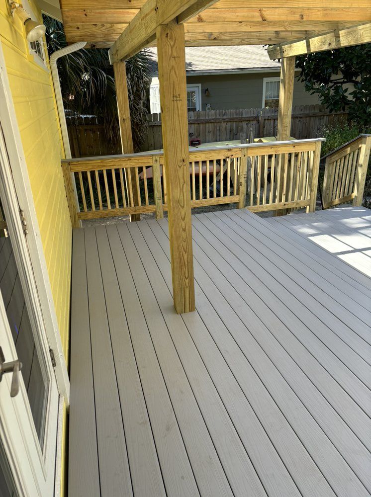 Covered wooden deck with gray flooring, yellow railing, and a support post overlooking a yard.