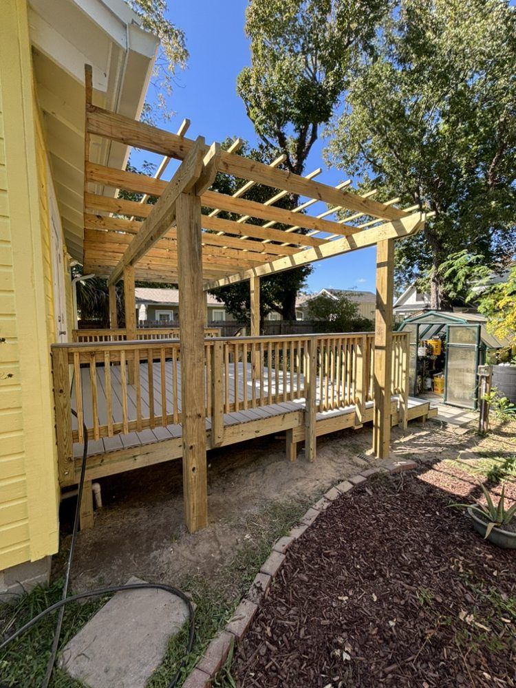 Wooden porch under construction beside a yellow house, with railings and open roof framing.