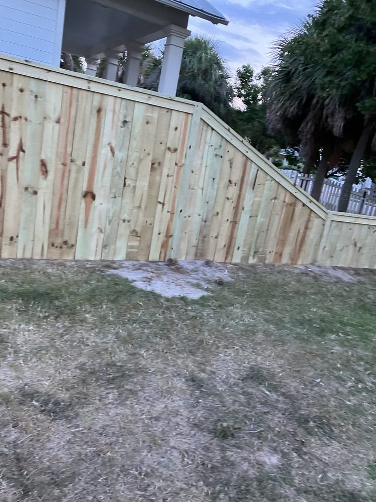 Wooden fence along a grassy yard beside a house, with trees in the background.