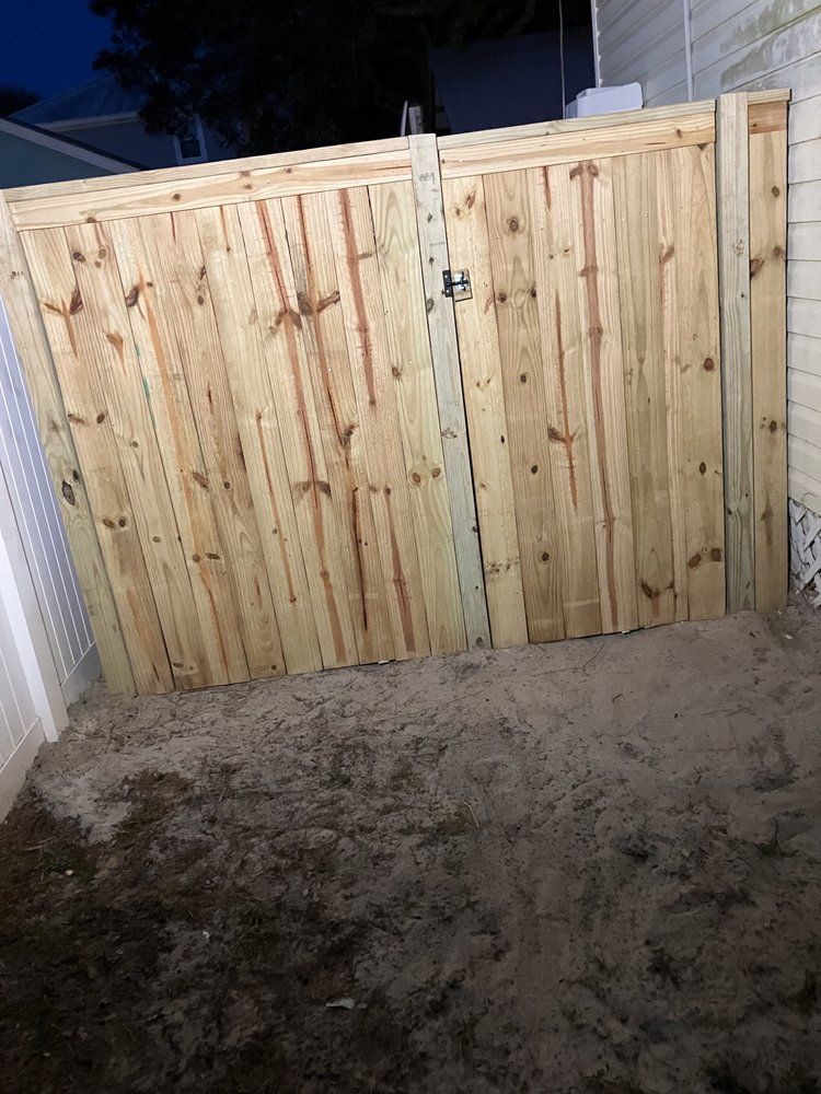 Wooden driveway gate with a metal latch, viewed at night on a gravel surface.