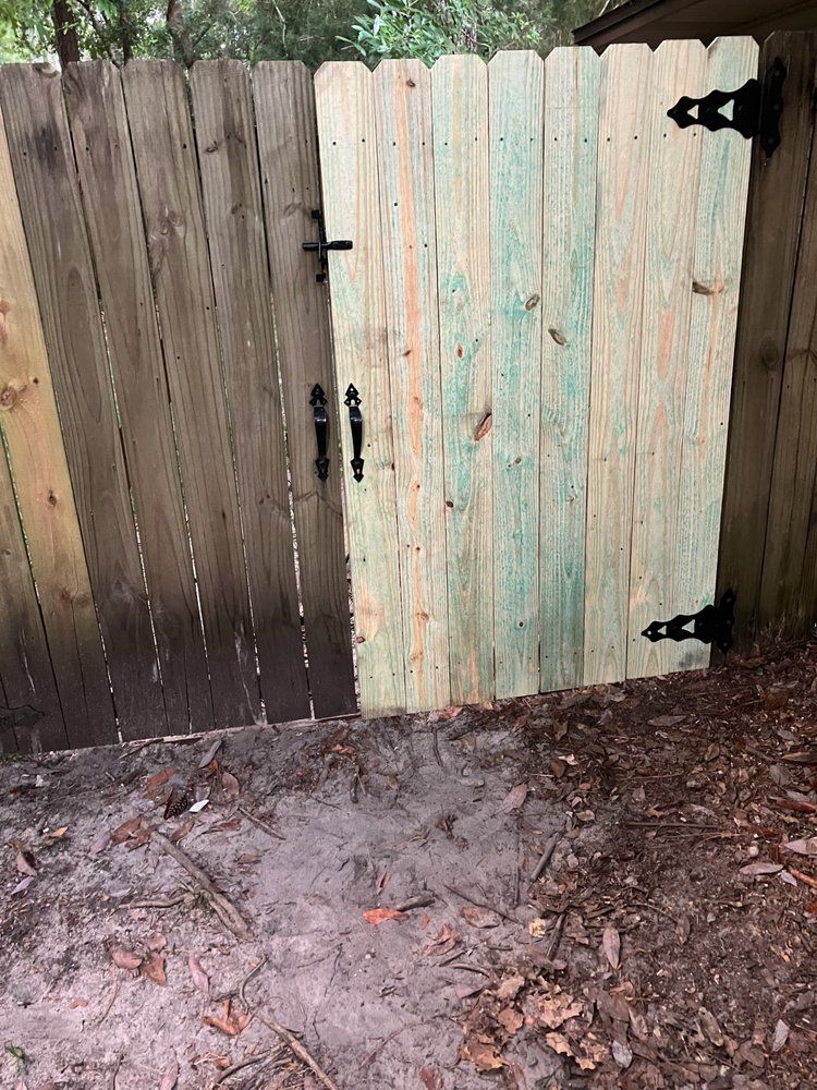 Weathered wooden gate with black hinges, one dark panel and one pale panel, over muddy ground with leaves