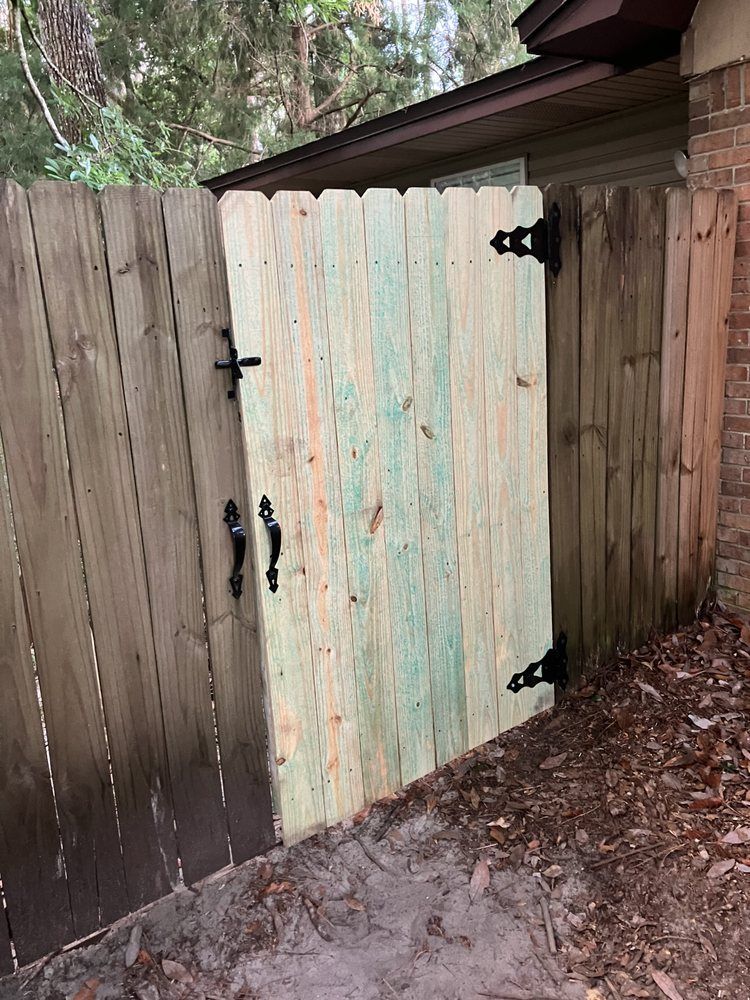Weathered wooden gate between fences, with black hinges and a pale turquoise center panel.