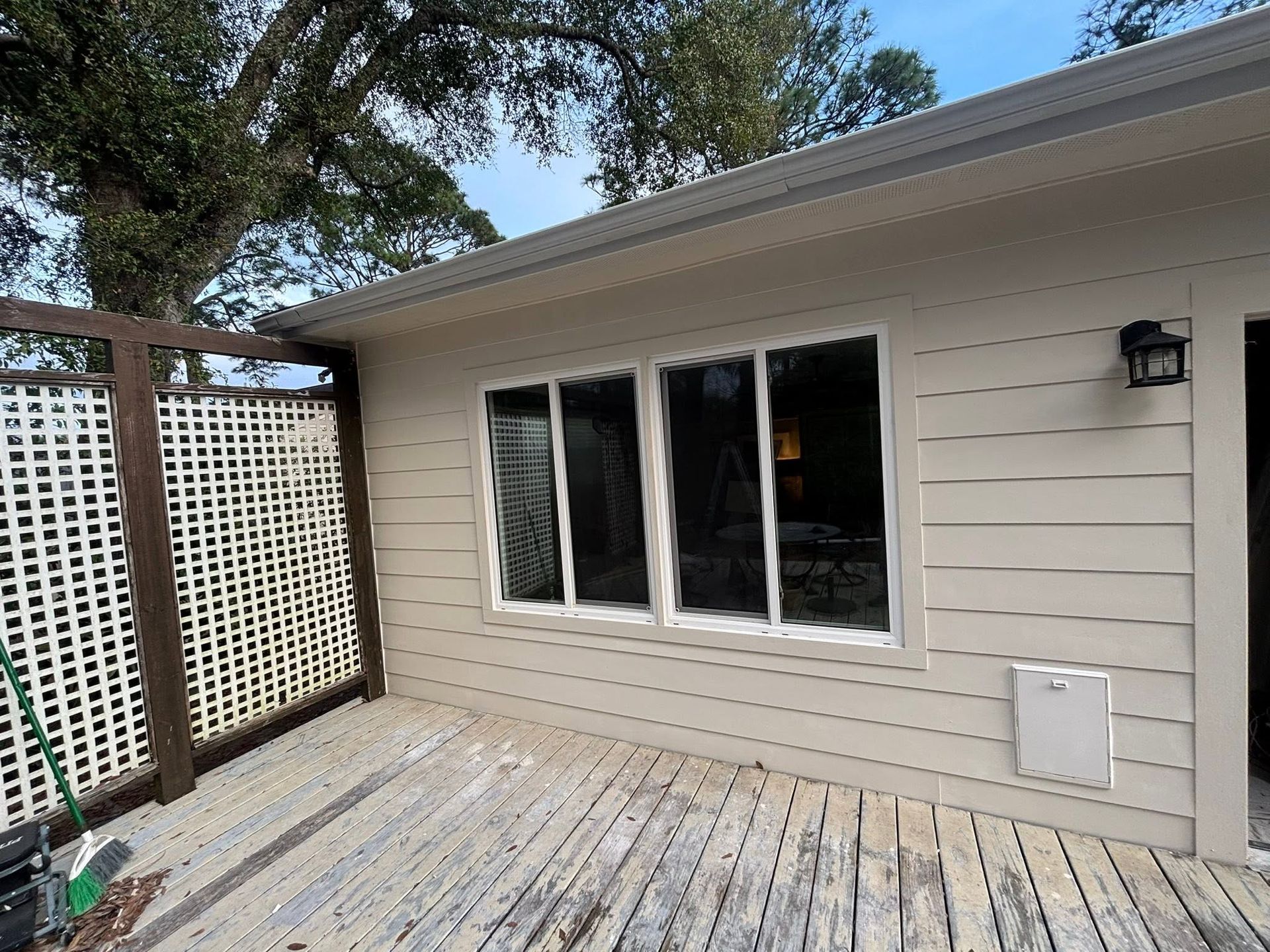 Back patio with beige siding, large window, lattice fence, and weathered wooden deck
