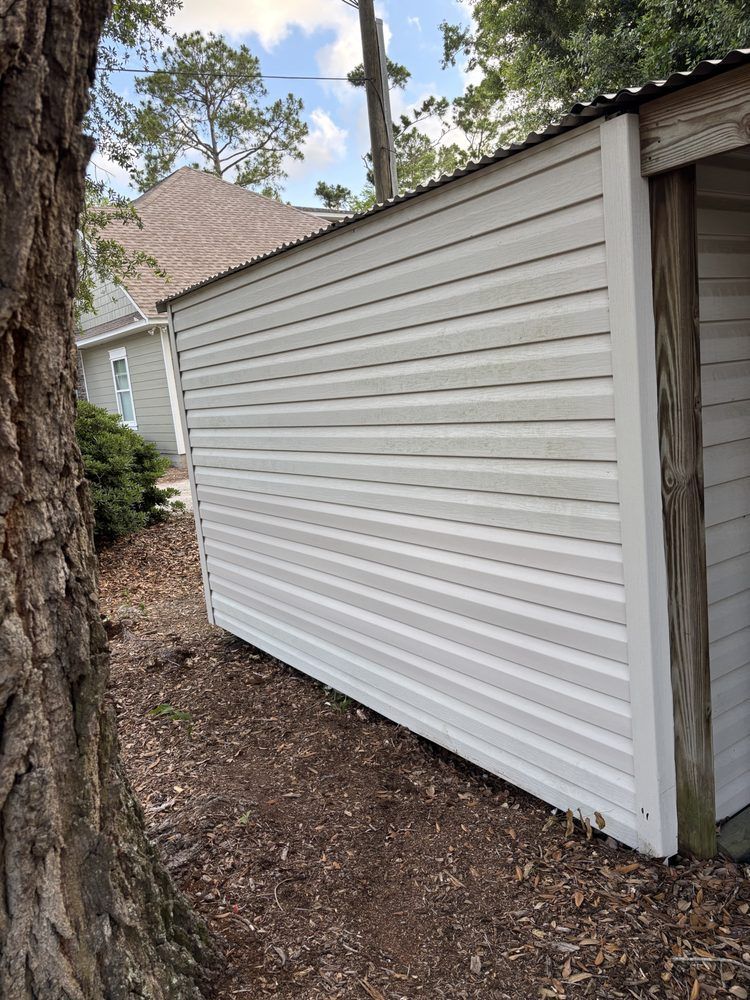 White vinyl-sided exterior wall of a house beside a tree and wooded yard
