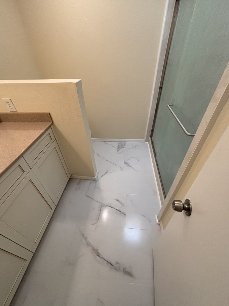 Narrow bathroom with vanity, frosted glass shower door, and marble-look tile floor