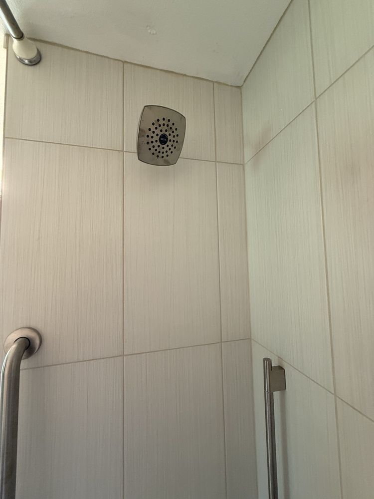 Tiled shower corner with wall-mounted showerhead and grab bars in a white bathroom