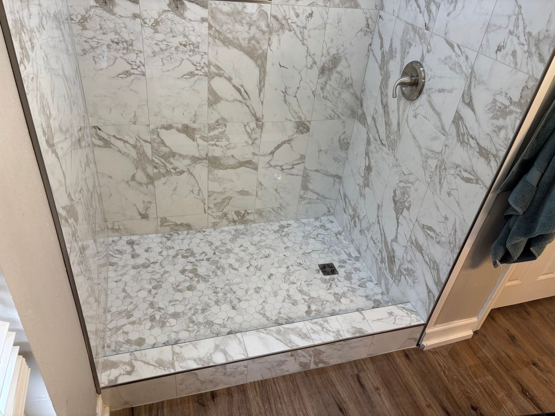 Walk-in shower with white marble tile, stone floor, and wood bathroom floor outside
