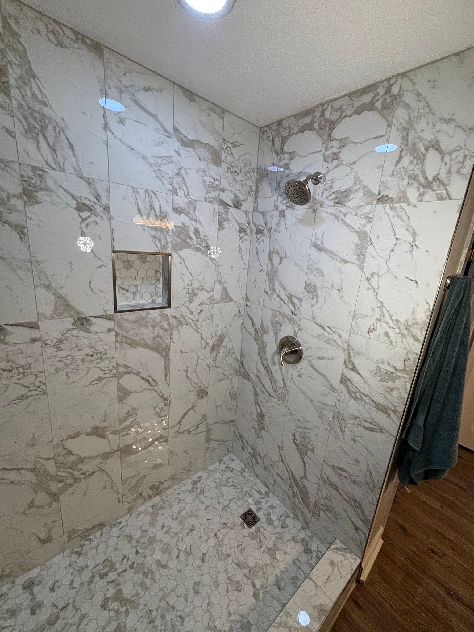 Empty tiled shower with marble-pattern walls, built-in niche, and glass door frame.