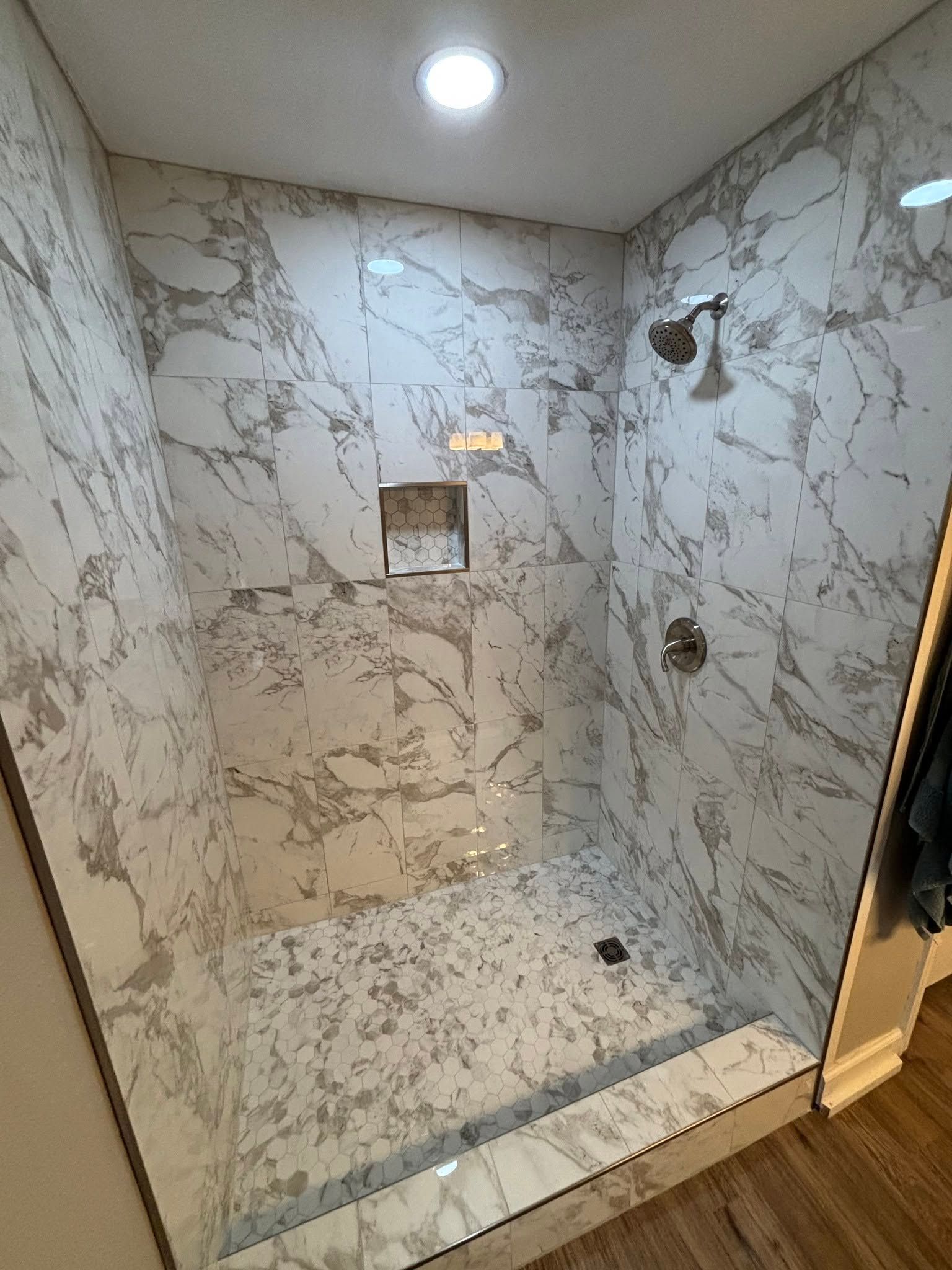 Marble-tiled walk-in shower with glass enclosure, built-in shelf, and recessed ceiling light