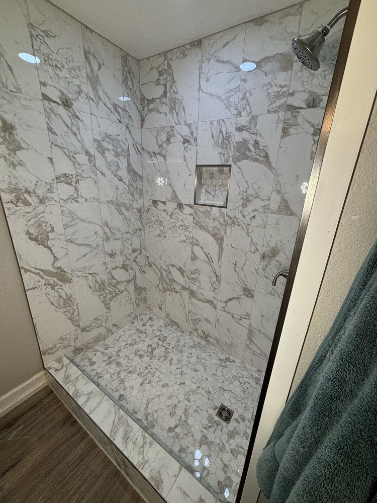 Marble-tiled walk-in shower with glass door and small recessed shelf