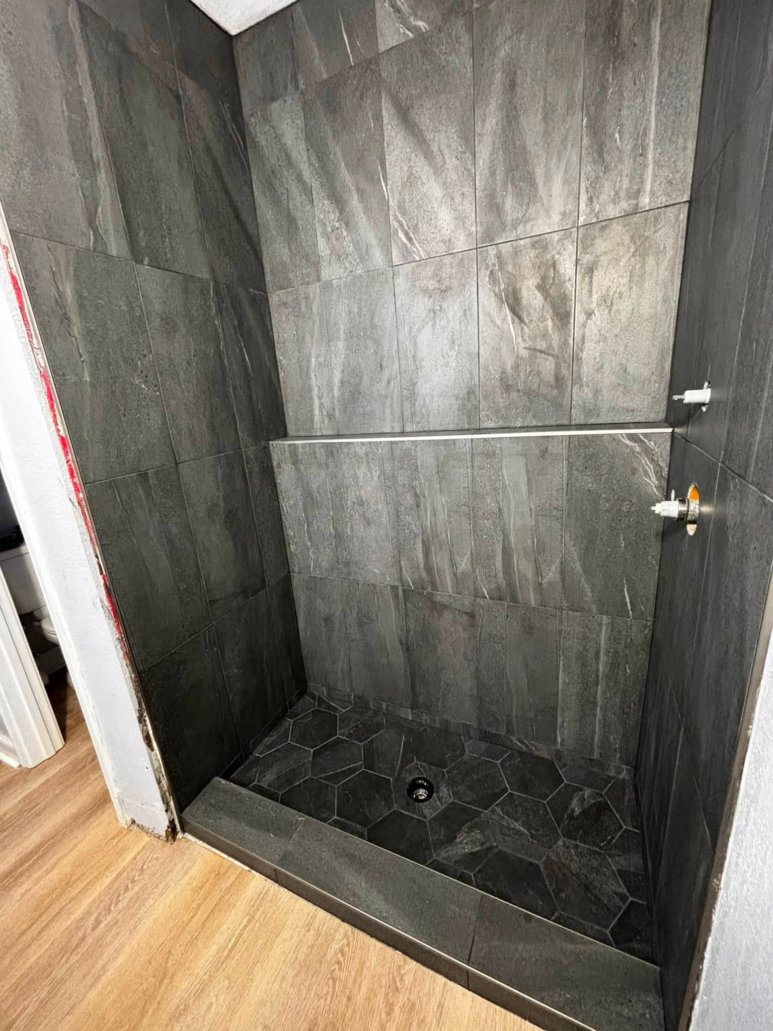Empty black-tiled walk-in shower with a low curb and a chrome shower valve on the right wall