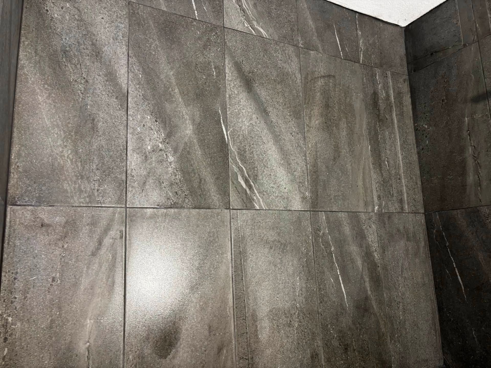 Gray tiled wall and floor corner with a bright white ceiling edge.