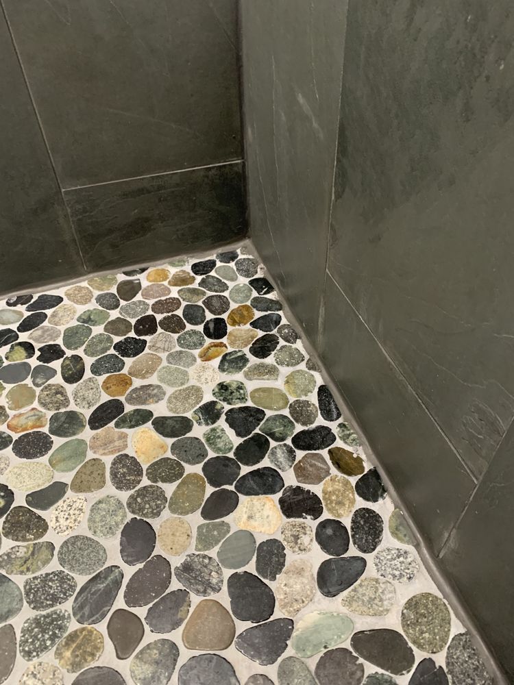 Corner of a shower with gray walls and a pebble mosaic floor.