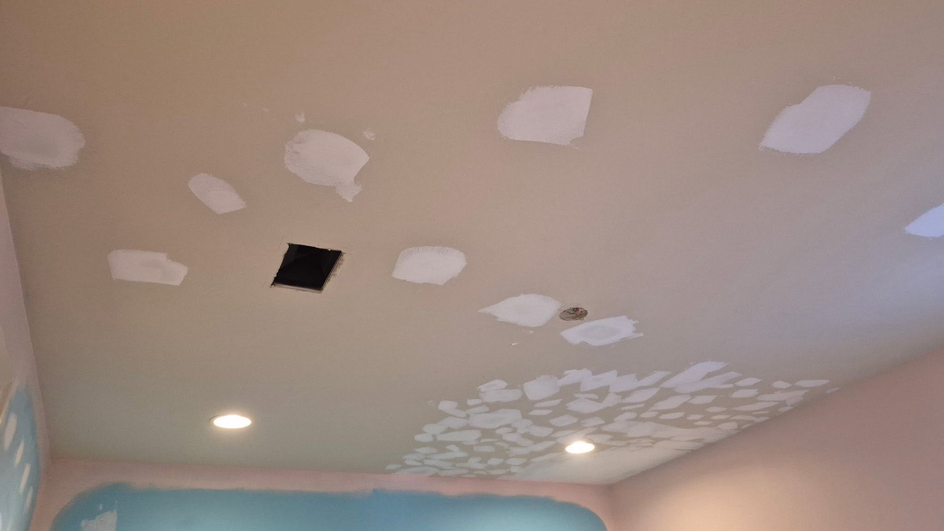 Ceiling with white patch repairs, one open black vent, and recessed lights in a room