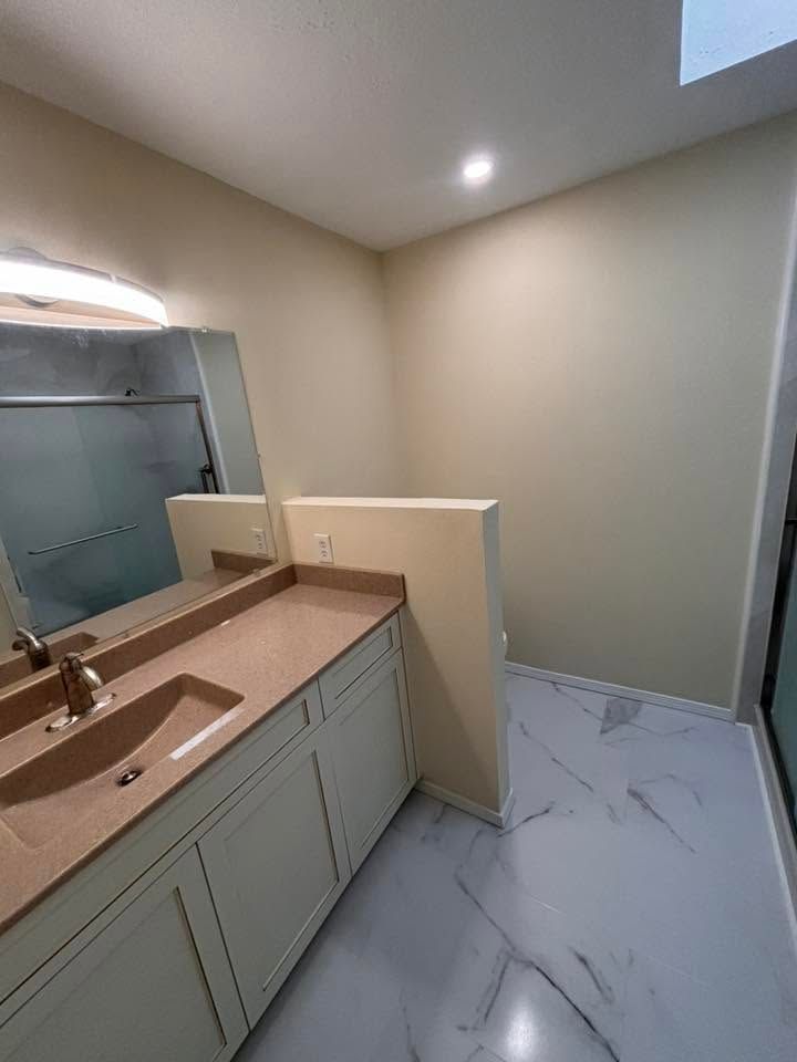 Empty bathroom vanity with beige walls, marble-look floor, and a large mirror.