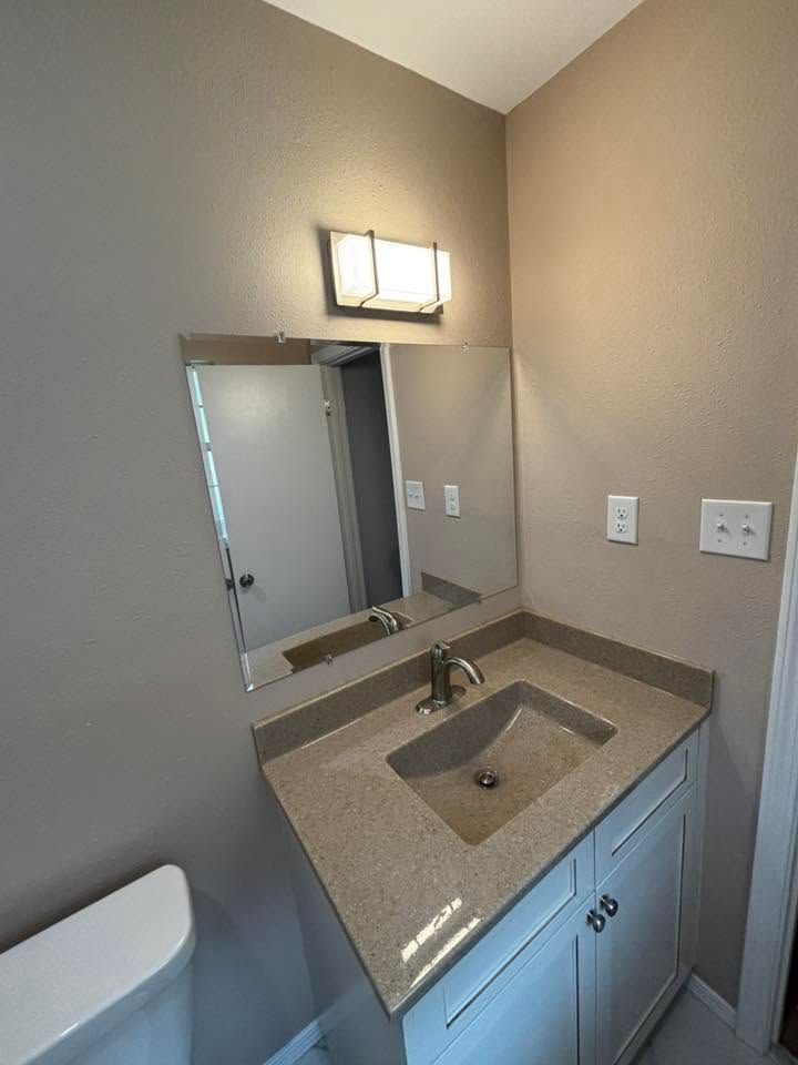 Small bathroom vanity with mirror, light fixture, sink, beige walls, and white cabinet.