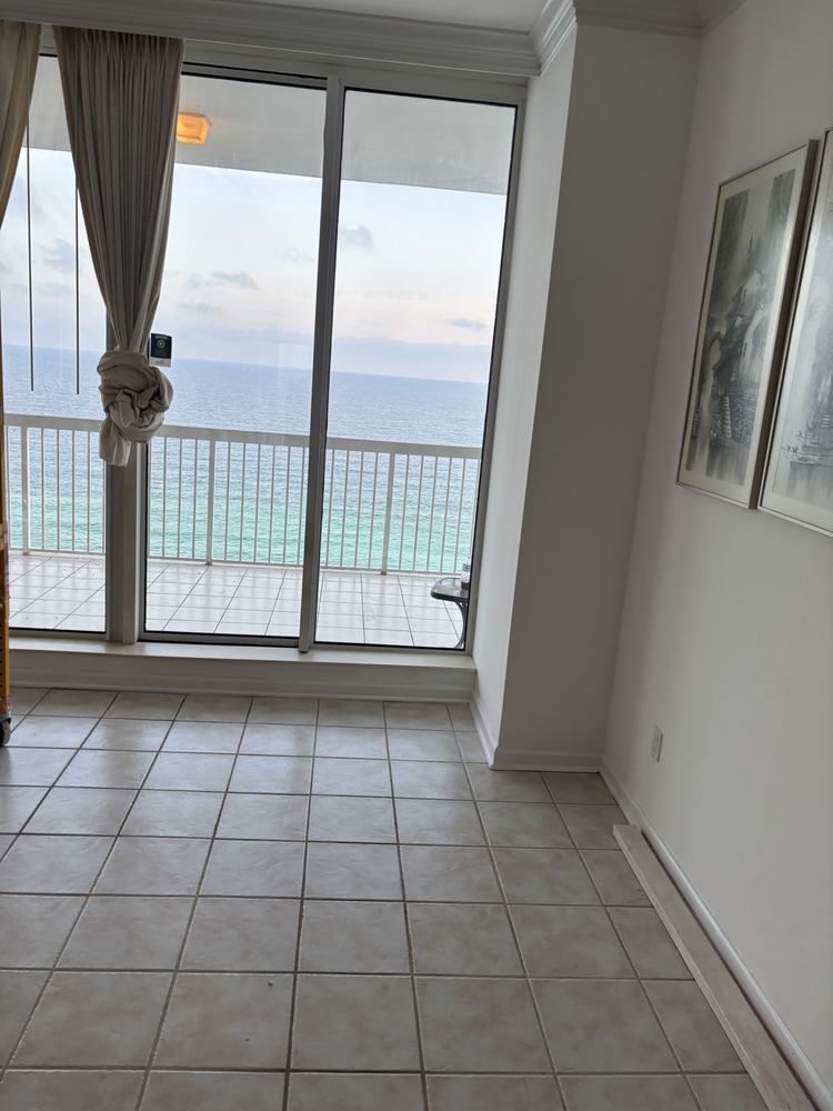 Empty tiled room with sliding glass doors, curtains, and a balcony view of the ocean.