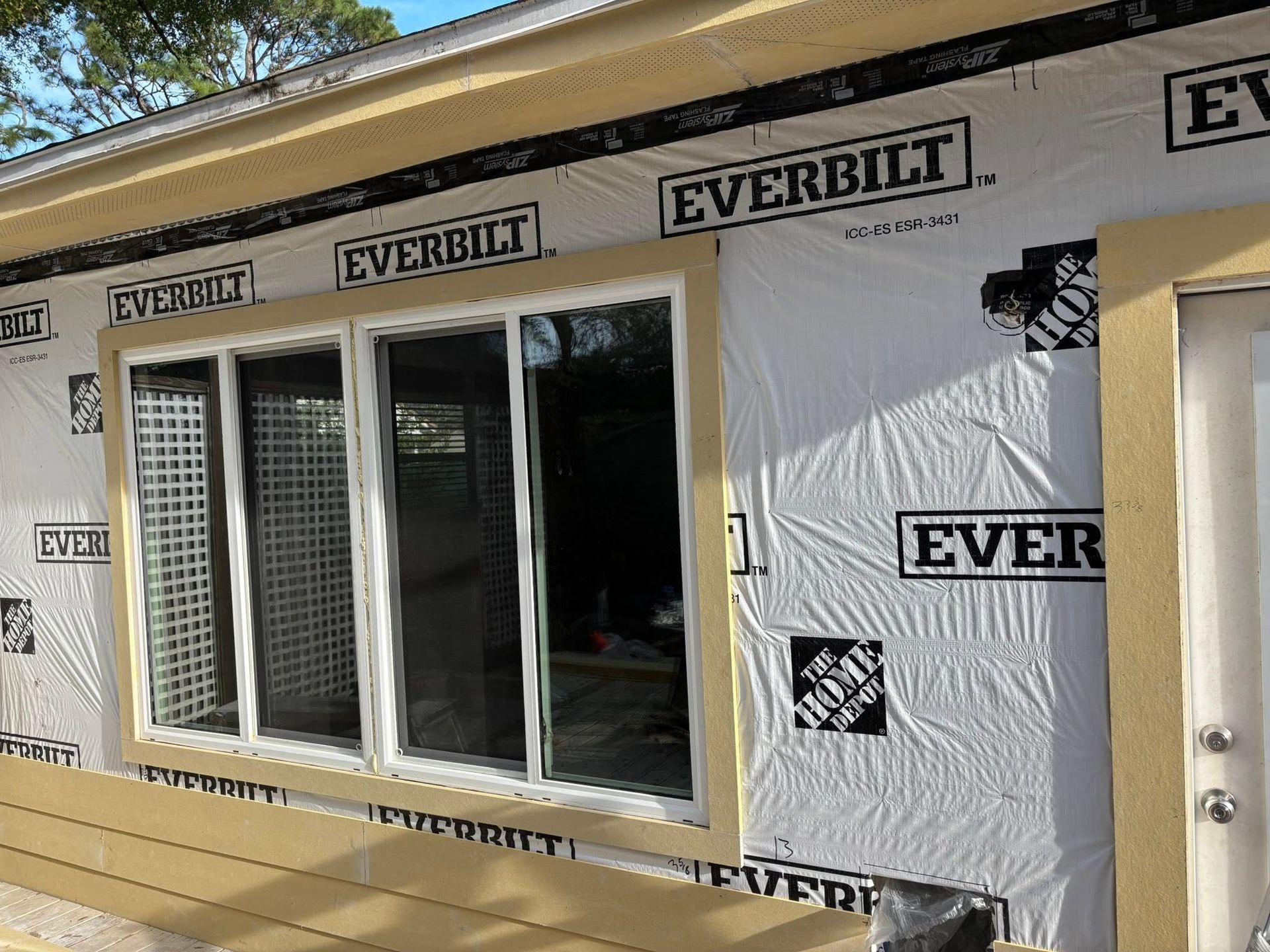 House wall under construction with wrapped siding, a window, and a front door under sunlight