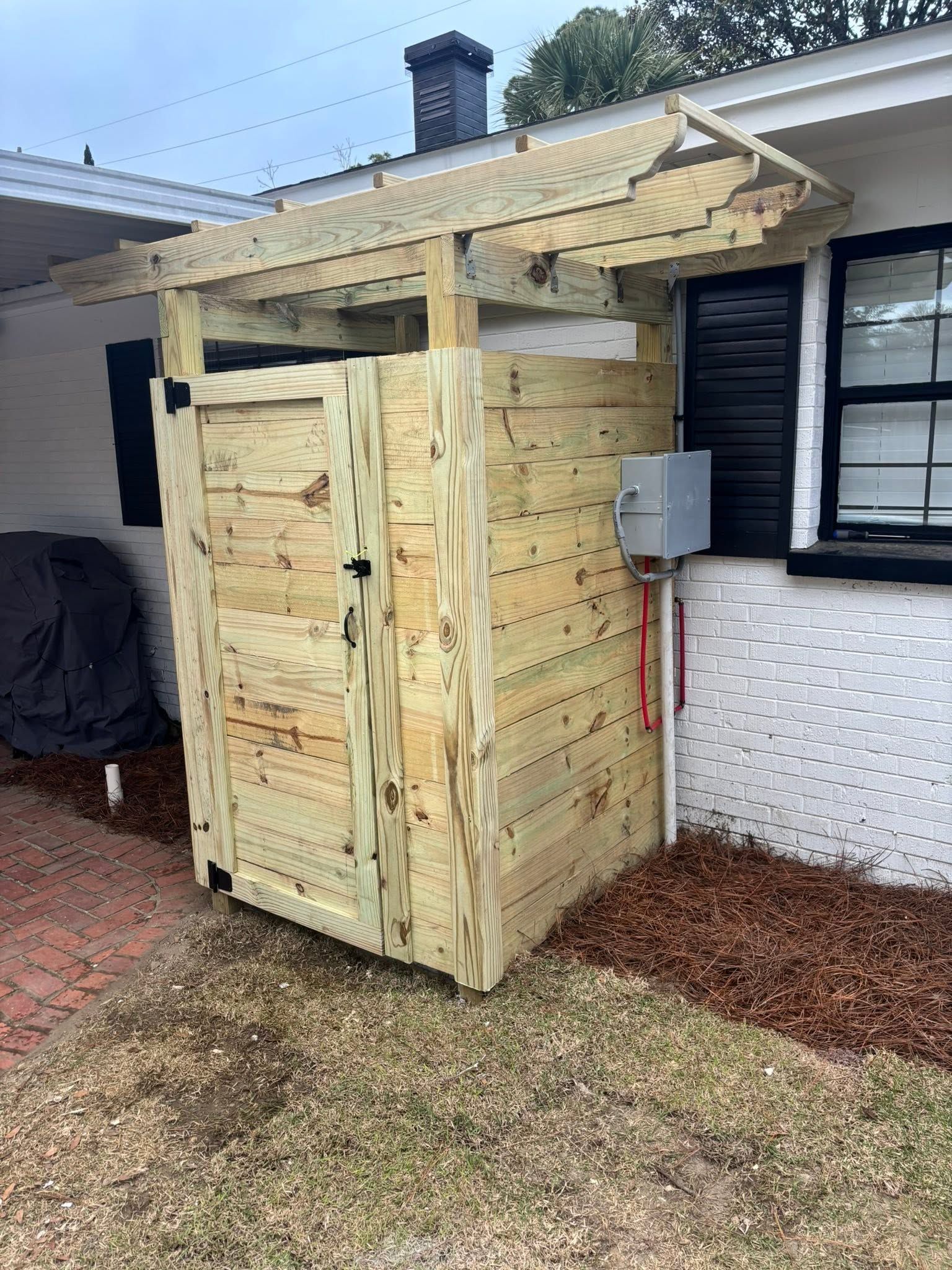 Wooden outdoor storage shed beside a house, with a slanted roof and white siding background