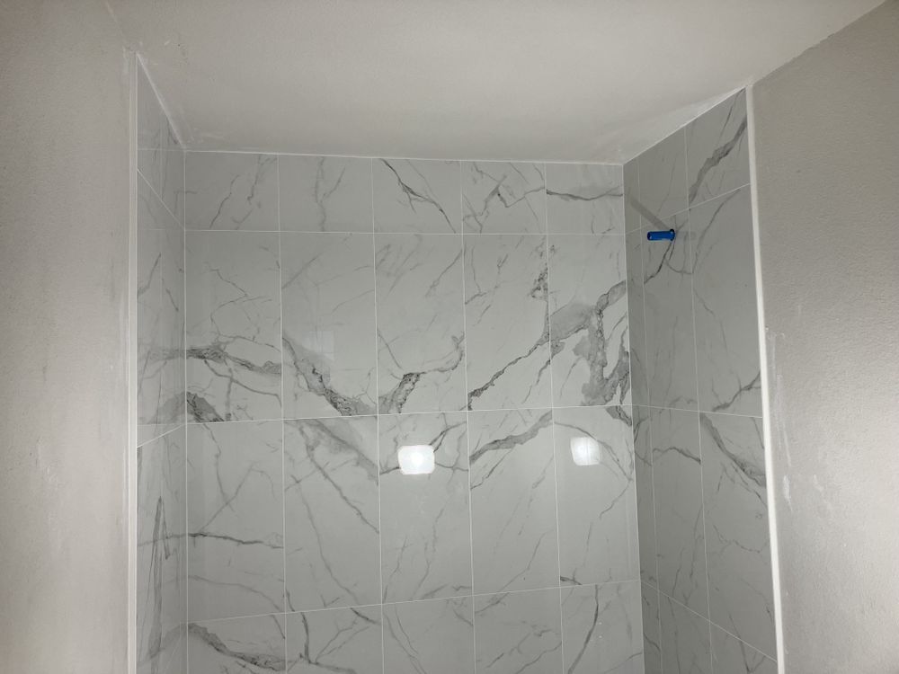 White-tiled shower stall with marble-pattern walls and a small blue shower fixture on the right.