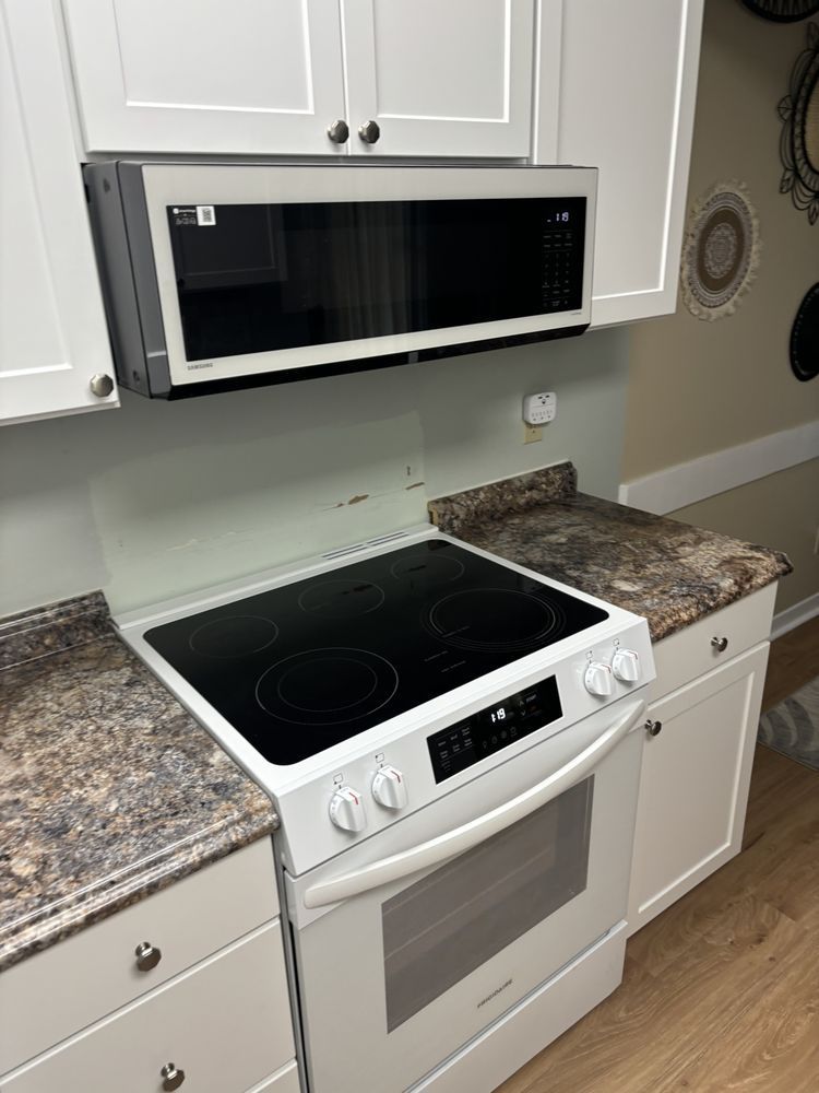 White kitchen with black microwave, white stove, and granite countertops in front of white cabinets
