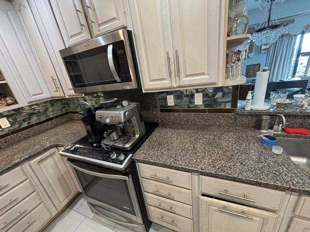 Bright kitchen with white cabinets, granite counters, stainless stove and microwave, and a coffee maker on the counter