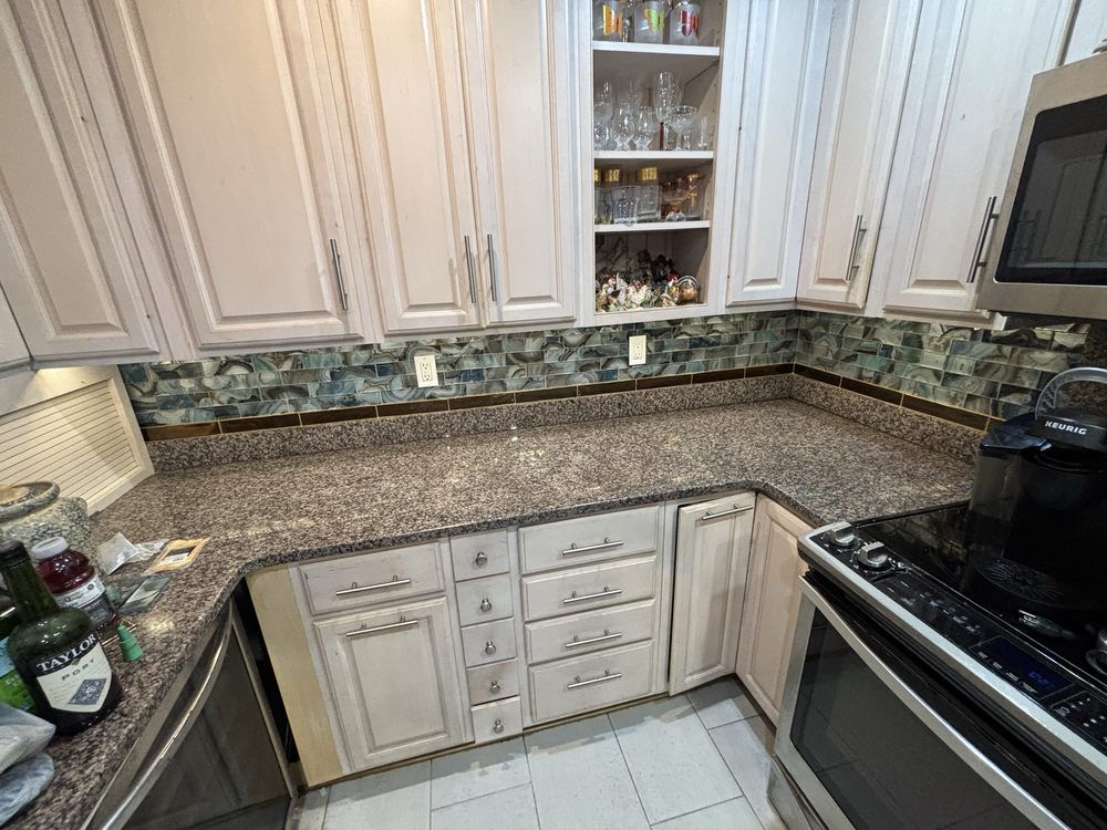 Kitchen with white cabinets, speckled granite counters, and black stove beside a sink and backsplash.