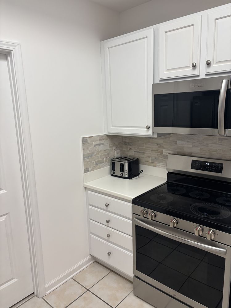 Small white kitchen with stainless steel oven and microwave, white cabinets, and a toaster on the counter.