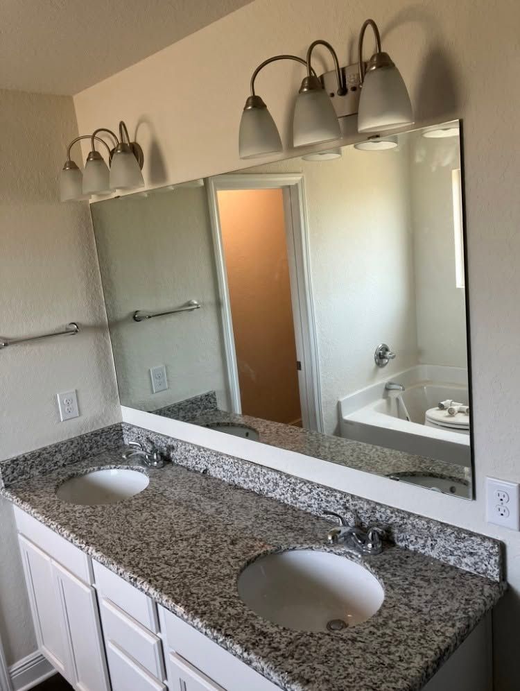 Bathroom vanity with two sinks, granite countertop, and large wall mirror above.