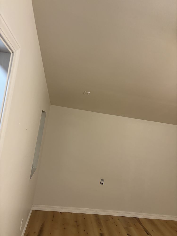 Empty beige room with white trim, a window on the left, and wood flooring.
