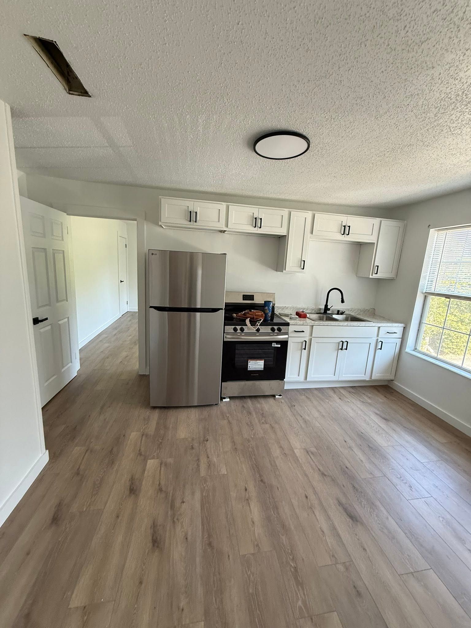Empty kitchen with stainless steel fridge, white cabinets, black stove, and wood-look flooring.