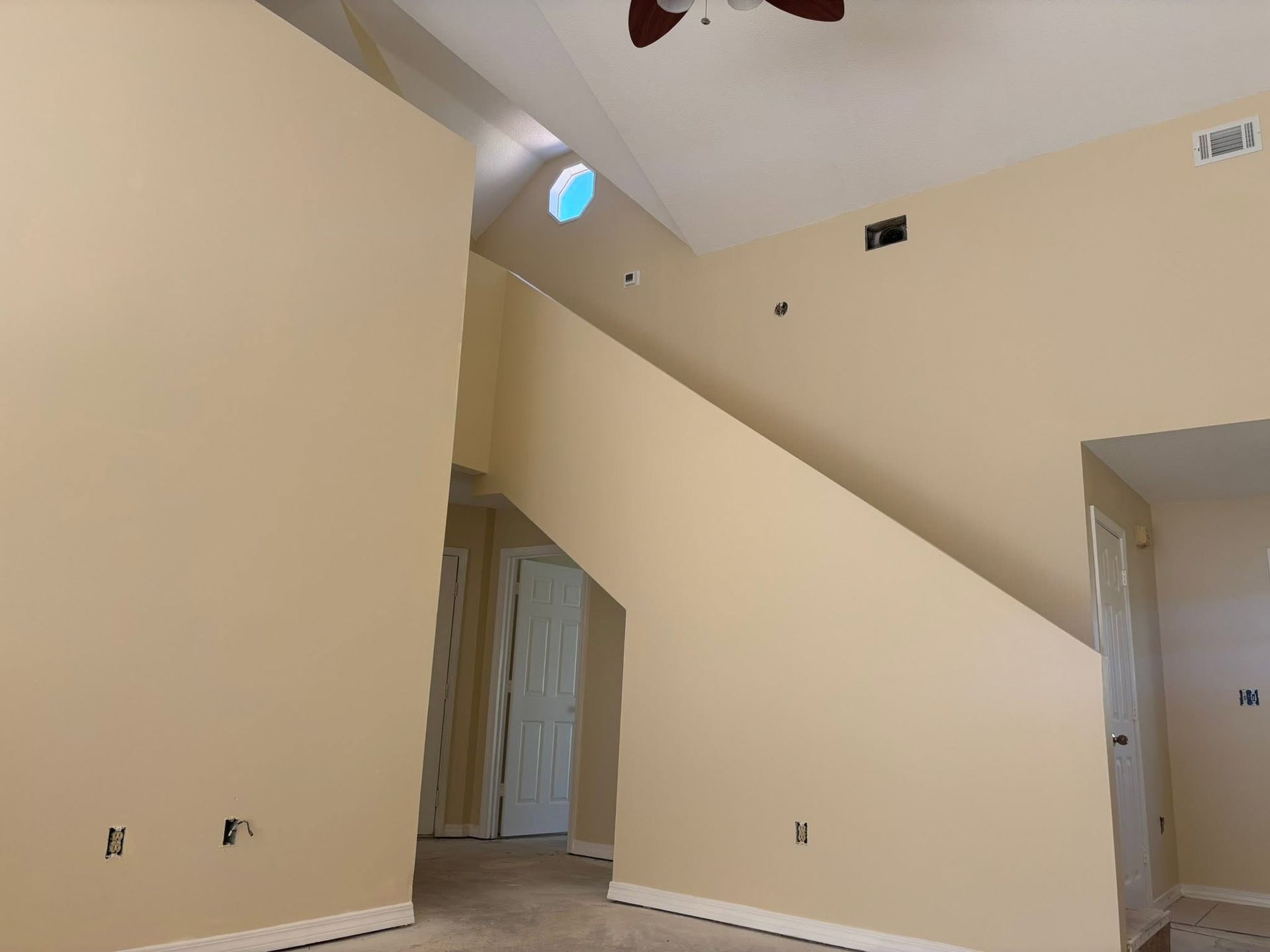 Empty beige room with sloped ceiling, central diagonal wall, doorways, and blue skylight.