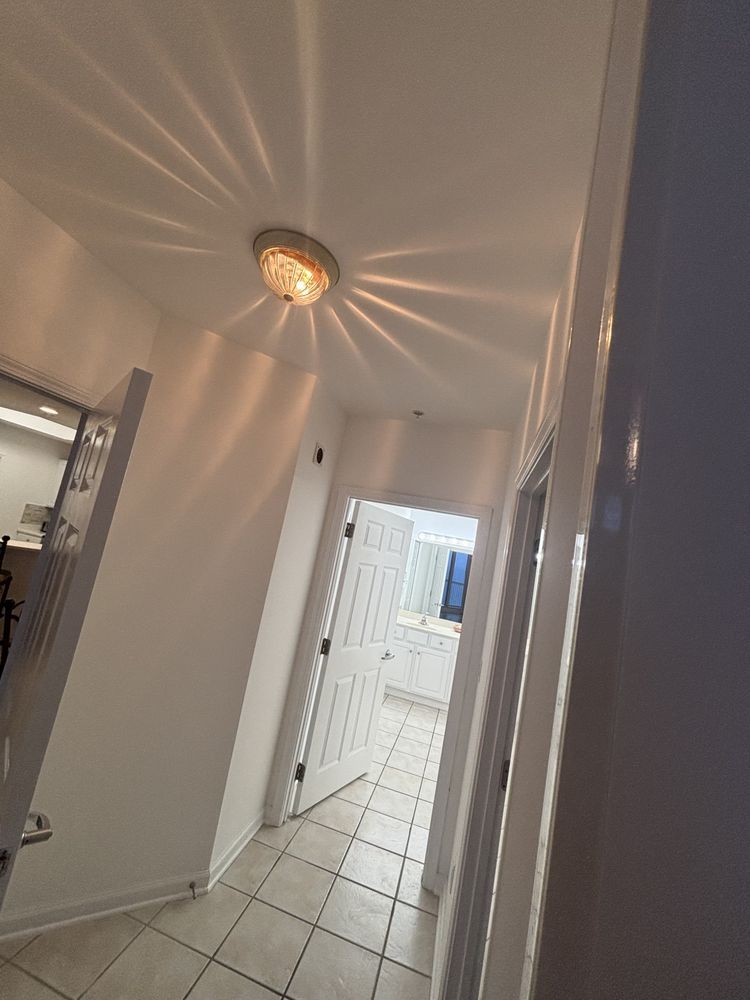 Narrow white hallway with tiled floor, ceiling light, and open doors leading to a bright entryway