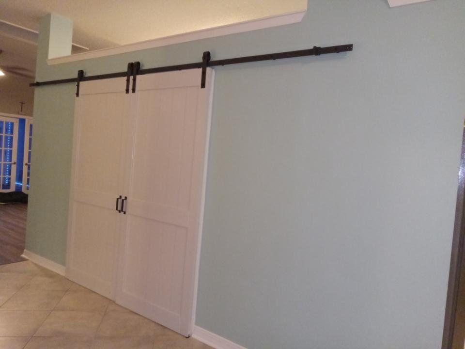 White sliding barn doors with black hardware on a pale green wall in a tiled hallway
