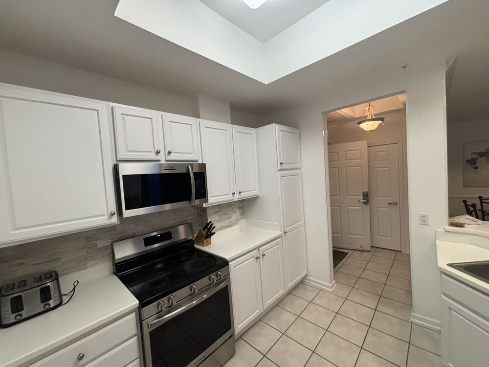 Bright white kitchen with black stove and microwave, tiled floor, and skylight ceiling.