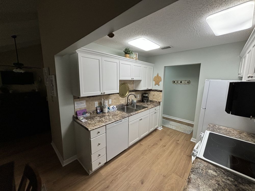 Bright kitchen with white cabinets, granite counters, wood floor, and overhead lights.