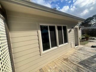 Beige house exterior with large windows and a weathered wooden deck under a partly cloudy sky