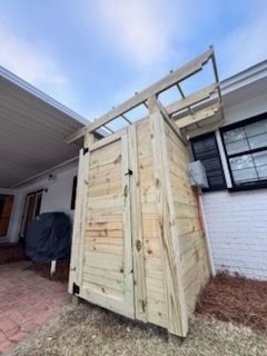 Wooden outdoor cabinet or shed beside a house, with open doors and a slanted top frame.