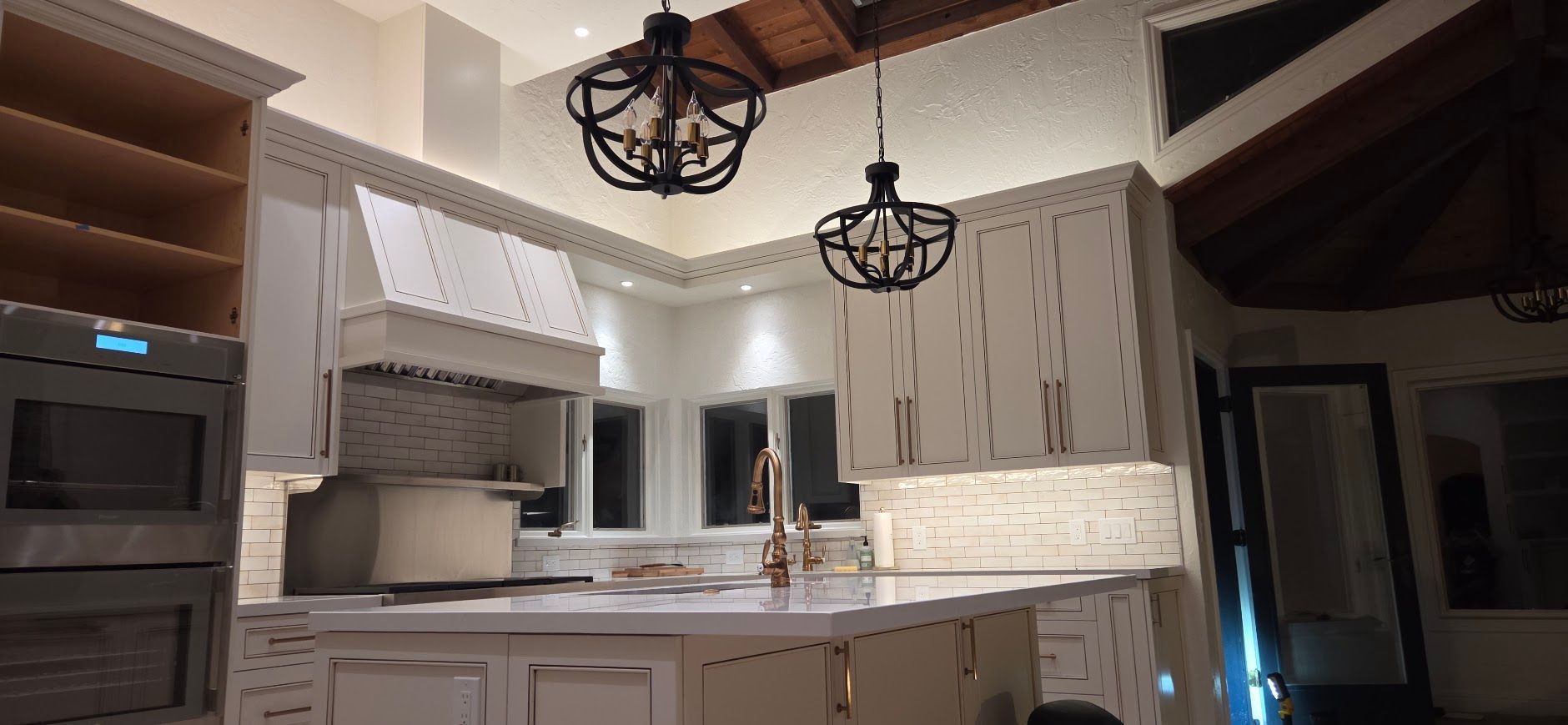 Modern kitchen with white cabinets, marble countertops, and two black pendant lights under a vaulted ceiling