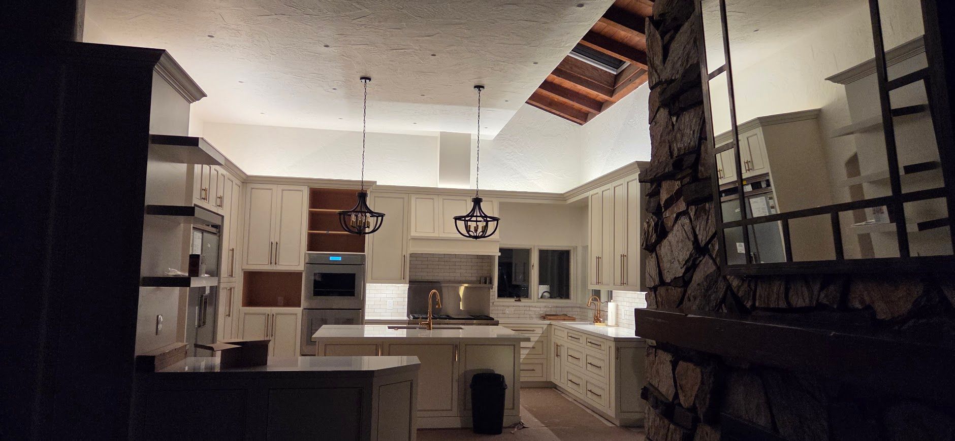 Dim kitchen under renovation with white cabinets, exposed ceiling, and a dark countertop in the foreground